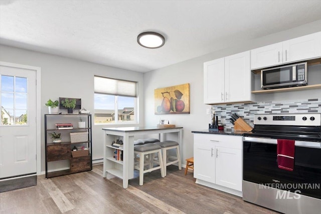 kitchen featuring dark countertops, light wood-style flooring, stainless steel appliances, white cabinetry, and backsplash