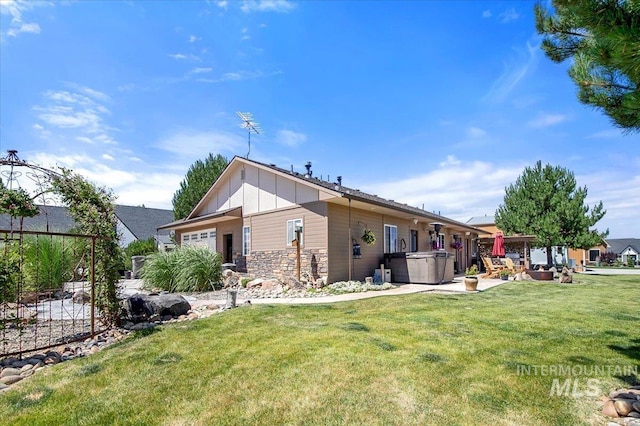 rear view of house with fence, stone siding, a lawn, board and batten siding, and a patio area