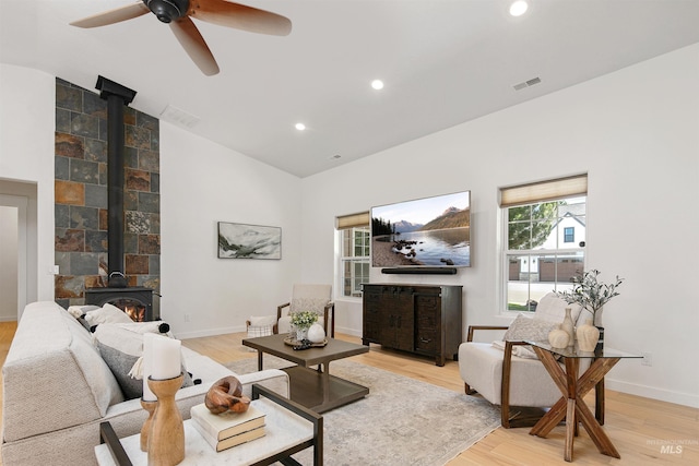 living area featuring a wood stove, light wood-type flooring, visible vents, and vaulted ceiling