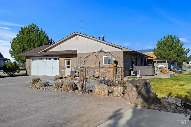 single story home with a hot tub, an attached garage, central AC unit, stone siding, and driveway