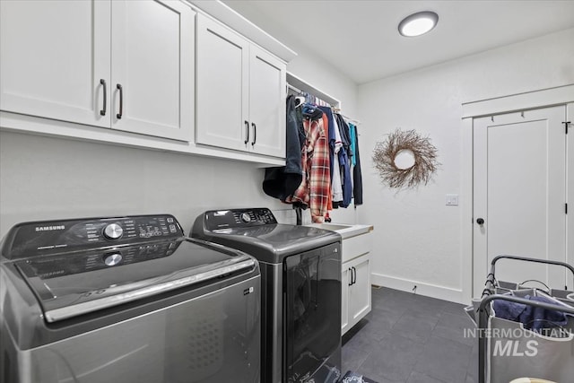 washroom featuring cabinet space, separate washer and dryer, baseboards, and dark tile patterned flooring