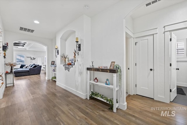 hall with visible vents, arched walkways, wood finished floors, and a wealth of natural light