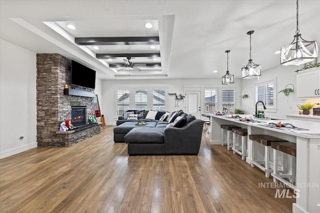 living room with ceiling fan, wood-type flooring, a stone fireplace, plenty of natural light, and a tray ceiling