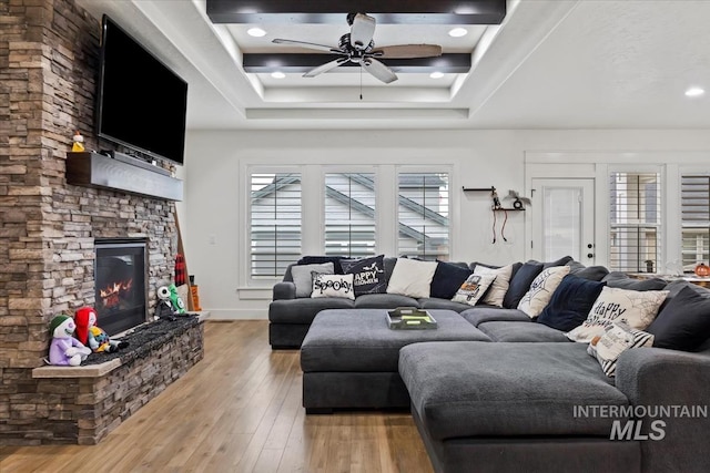 living room featuring light wood-type flooring, a ceiling fan, a tray ceiling, and a fireplace