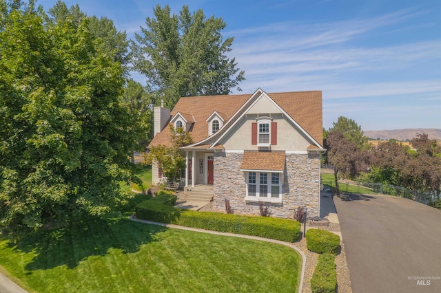 view of front facade featuring a chimney, stucco siding, fence, stone siding, and a front lawn