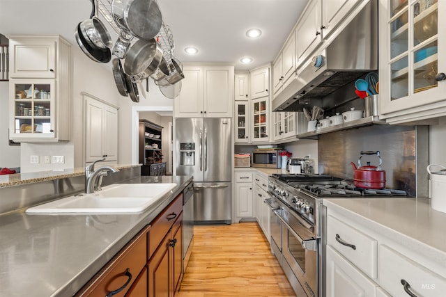 kitchen with brown cabinets, stainless steel countertops, appliances with stainless steel finishes, a sink, and under cabinet range hood