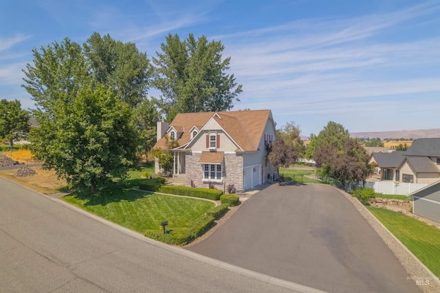 view of front of house featuring aphalt driveway, an attached garage, fence, stone siding, and a front lawn