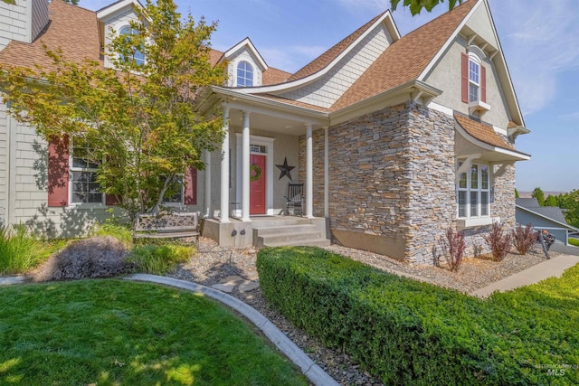 view of exterior entry with a shingled roof, stone siding, and a lawn