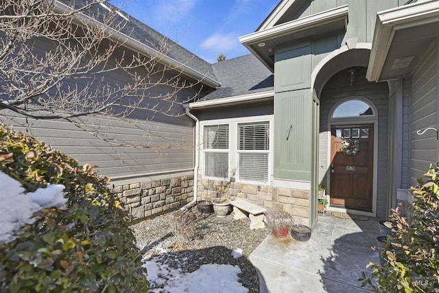 doorway to property featuring stone siding and a shingled roof