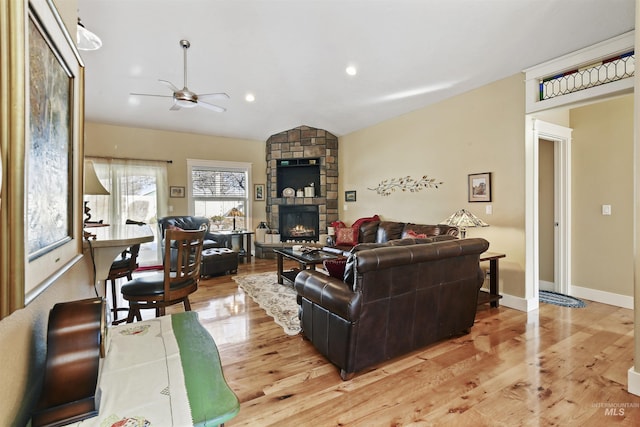 living room featuring light wood finished floors, baseboards, ceiling fan, vaulted ceiling, and a fireplace