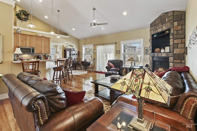 living area with a ceiling fan, light wood-type flooring, a fireplace, high vaulted ceiling, and recessed lighting