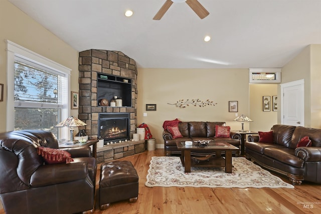 living area with ceiling fan, wood finished floors, vaulted ceiling, a stone fireplace, and recessed lighting