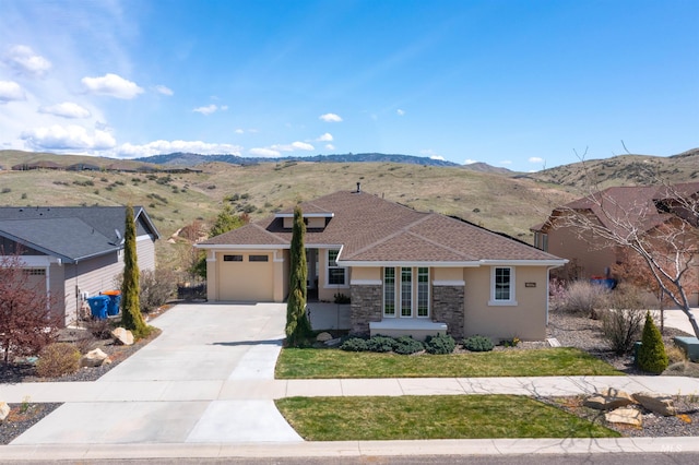 view of front of property featuring concrete driveway, stone siding, a mountain view, a garage, and stucco siding