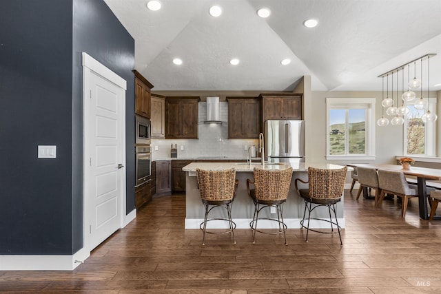 kitchen featuring lofted ceiling, stainless steel appliances, a breakfast bar, wall chimney exhaust hood, and a kitchen island with sink