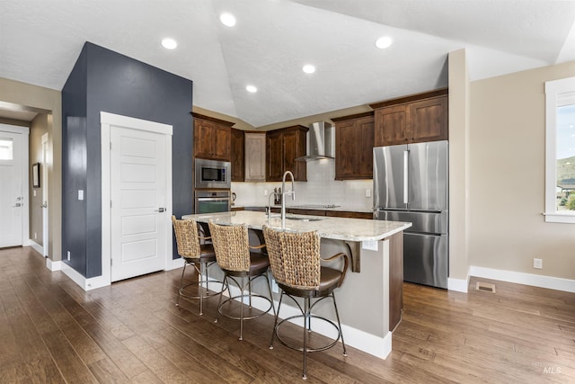 kitchen with wall chimney range hood, a sink, stainless steel appliances, a kitchen bar, and visible vents