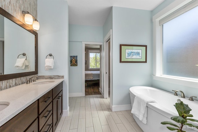 ensuite bathroom with a sink, ensuite bathroom, double vanity, a freestanding bath, and baseboards