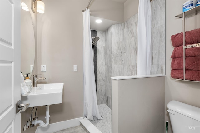 bathroom with toilet, baseboards, and tiled shower