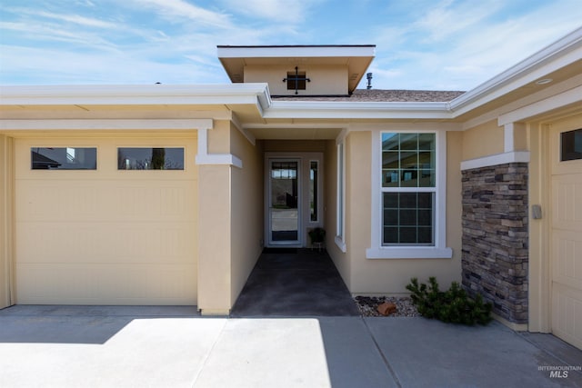 entrance to property featuring a garage, driveway, and stucco siding