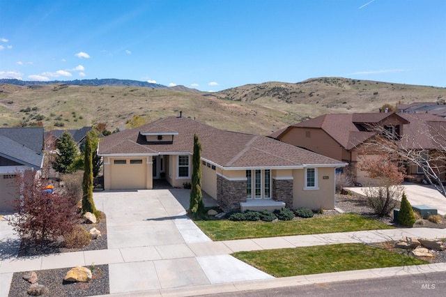 view of front of home with concrete driveway, stone siding, an attached garage, a mountain view, and stucco siding