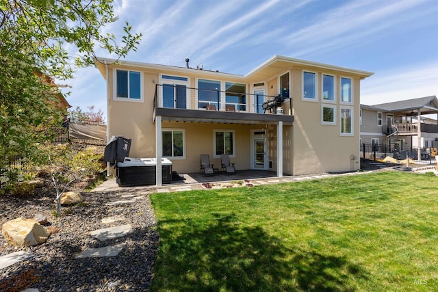 rear view of property featuring fence, a hot tub, a balcony, a yard, and stucco siding