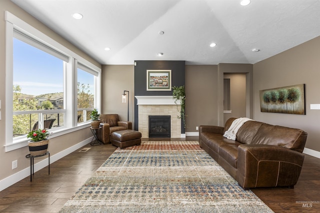 living room with dark wood finished floors, lofted ceiling, a tiled fireplace, and baseboards