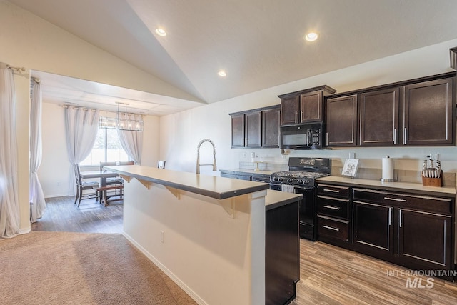 kitchen featuring vaulted ceiling, a kitchen bar, black appliances, dark brown cabinets, and a center island with sink