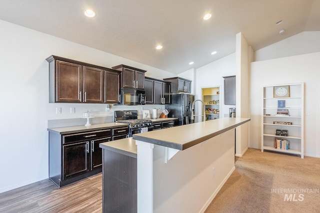 kitchen with lofted ceiling, a breakfast bar area, dark brown cabinets, an island with sink, and black appliances