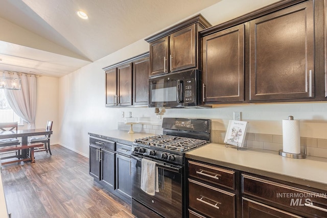 kitchen with dark brown cabinets, vaulted ceiling, black appliances, and dark hardwood / wood-style floors