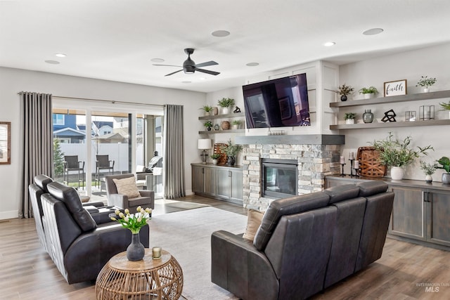 living room featuring ceiling fan, wood-type flooring, and a stone fireplace