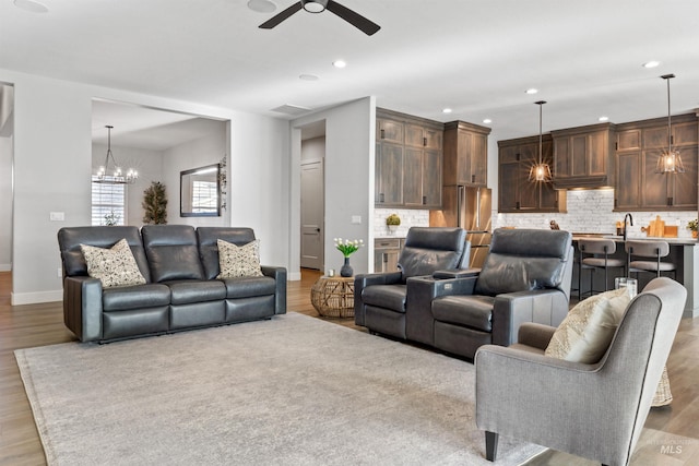 living room featuring ceiling fan with notable chandelier and light wood-type flooring