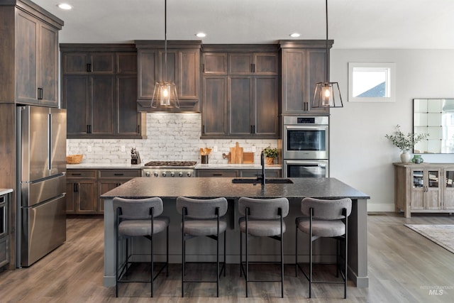 kitchen featuring appliances with stainless steel finishes, sink, hanging light fixtures, a kitchen island with sink, and dark brown cabinets