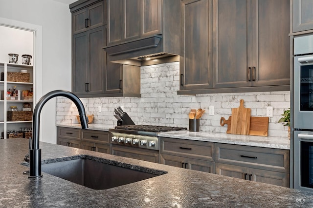 kitchen featuring custom exhaust hood, dark stone counters, sink, dark brown cabinets, and backsplash