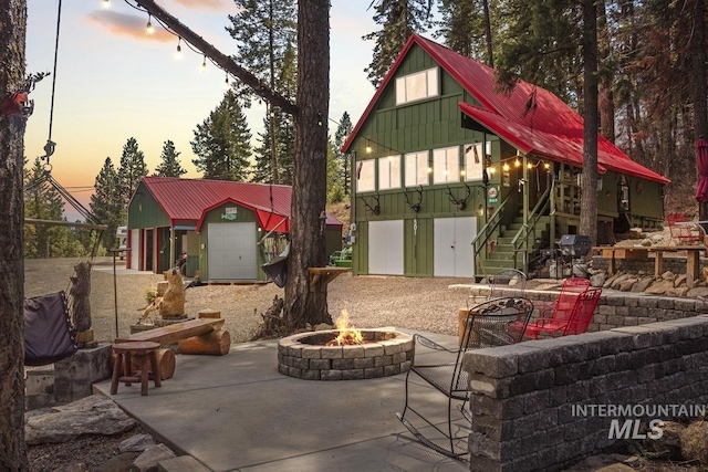 patio terrace at dusk featuring grilling area, a garage, stairway, an outdoor structure, and an outdoor fire pit