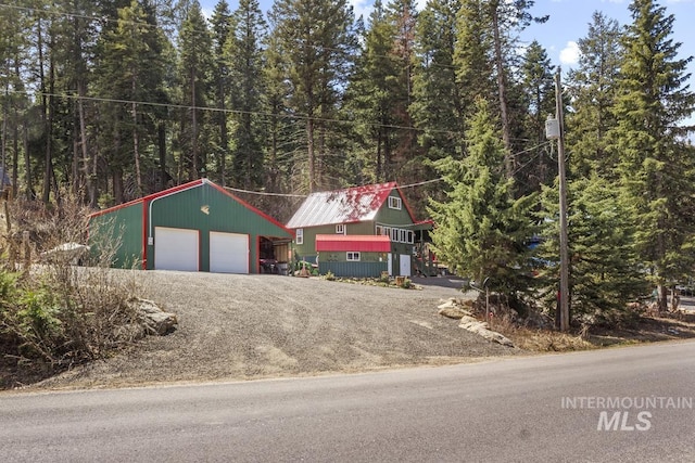 view of front of home featuring a detached garage, a forest view, driveway, and an outbuilding
