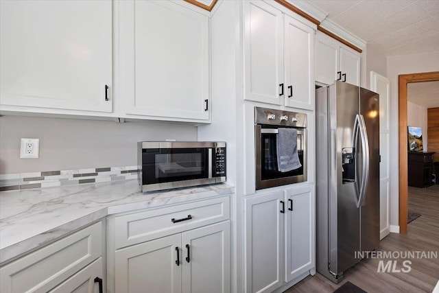 kitchen featuring light stone counters, white cabinetry, wood finished floors, and stainless steel appliances