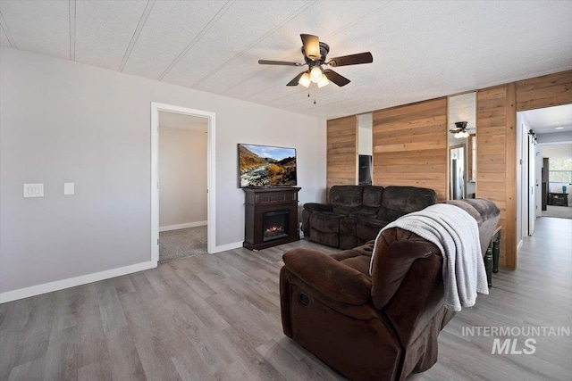 living area with a warm lit fireplace, ceiling fan, wood finished floors, and wooden walls