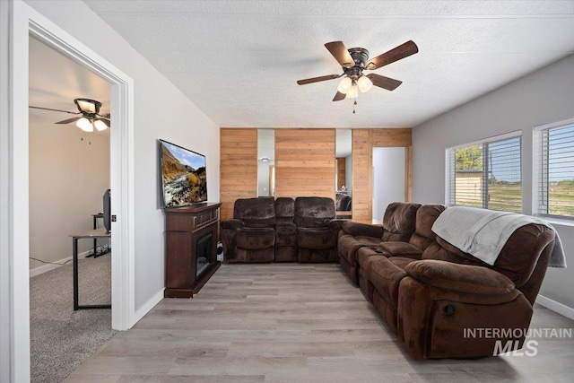 living room with a textured ceiling, light wood finished floors, ceiling fan, and wooden walls
