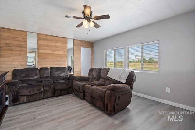 living area with a ceiling fan, wooden walls, light wood finished floors, and a wealth of natural light