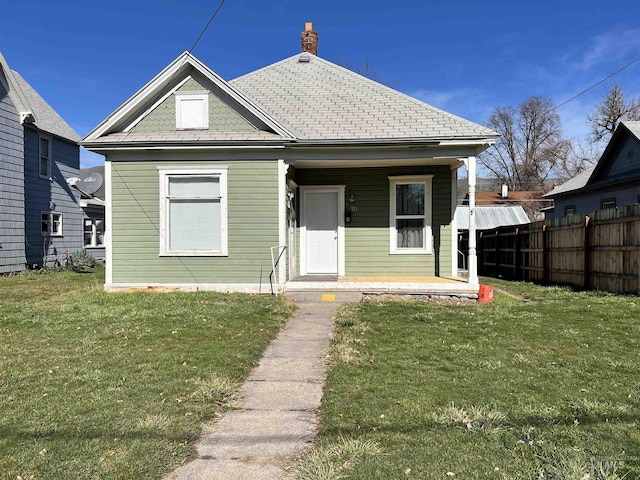 bungalow-style home with a front yard, fence, and a chimney