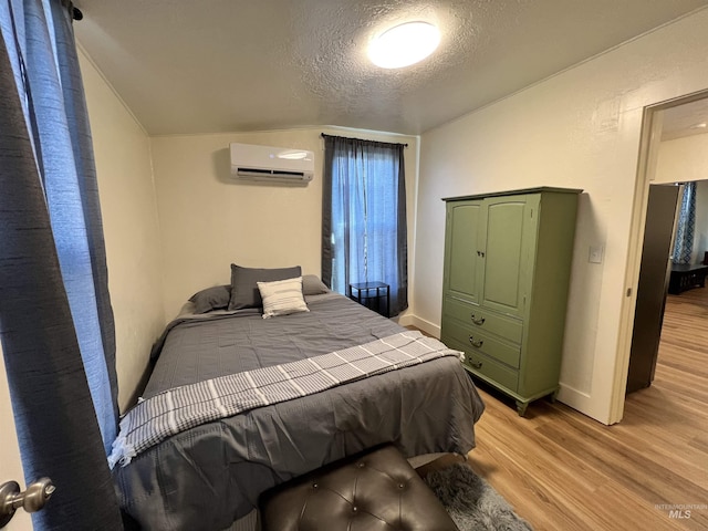 bedroom featuring a textured ceiling, baseboards, light wood-type flooring, and a wall mounted AC