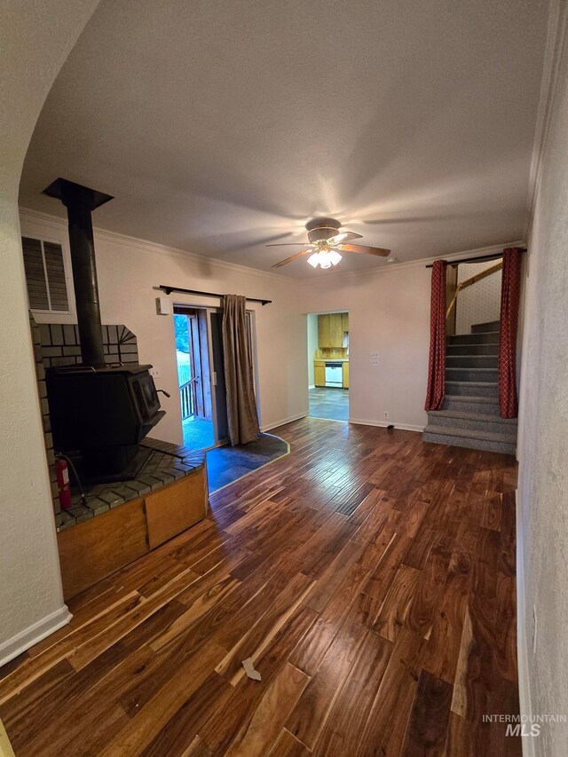 unfurnished living room with a wood stove, ornamental molding, ceiling fan, wood-type flooring, and a textured ceiling