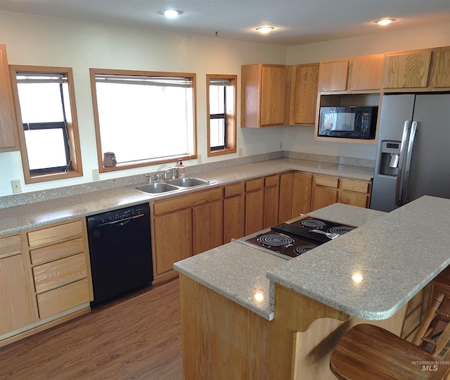 kitchen with light hardwood / wood-style flooring, black appliances, a kitchen bar, and a wealth of natural light