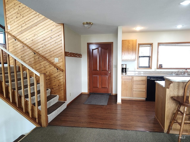 kitchen featuring dark hardwood / wood-style flooring, a kitchen breakfast bar, wood walls, dishwasher, and sink