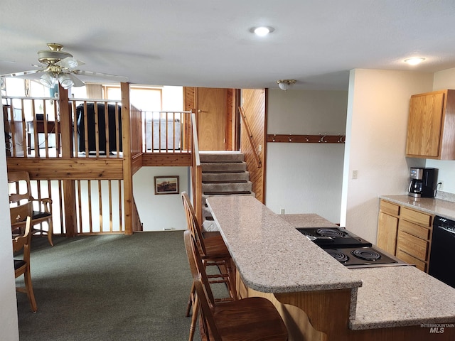 kitchen with ceiling fan, carpet, a kitchen island, and a kitchen breakfast bar