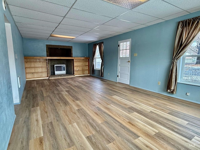 unfurnished living room with a large fireplace, a drop ceiling, and wood finished floors