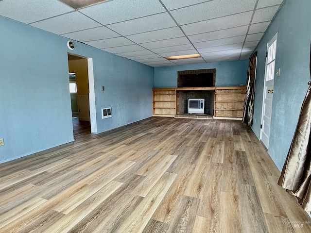 unfurnished living room featuring a drop ceiling, a fireplace, wood finished floors, visible vents, and heating unit