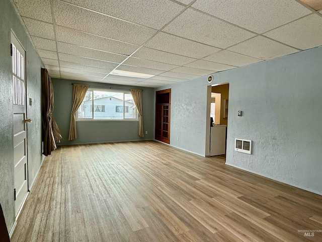 spare room featuring a textured wall, light wood-type flooring, a drop ceiling, and visible vents