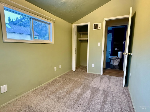 unfurnished bedroom featuring lofted ceiling, a closet, light colored carpet, a textured ceiling, and baseboards