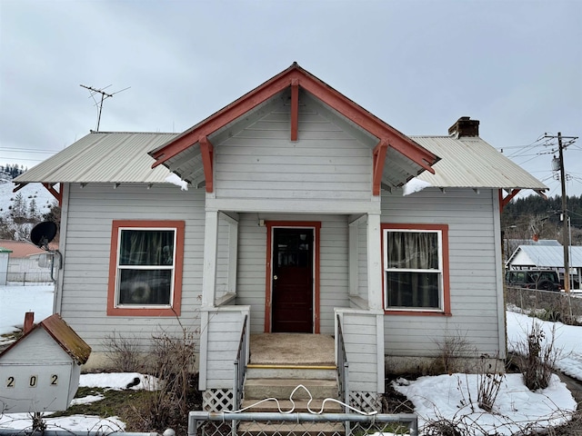 bungalow featuring metal roof, a chimney, and fence