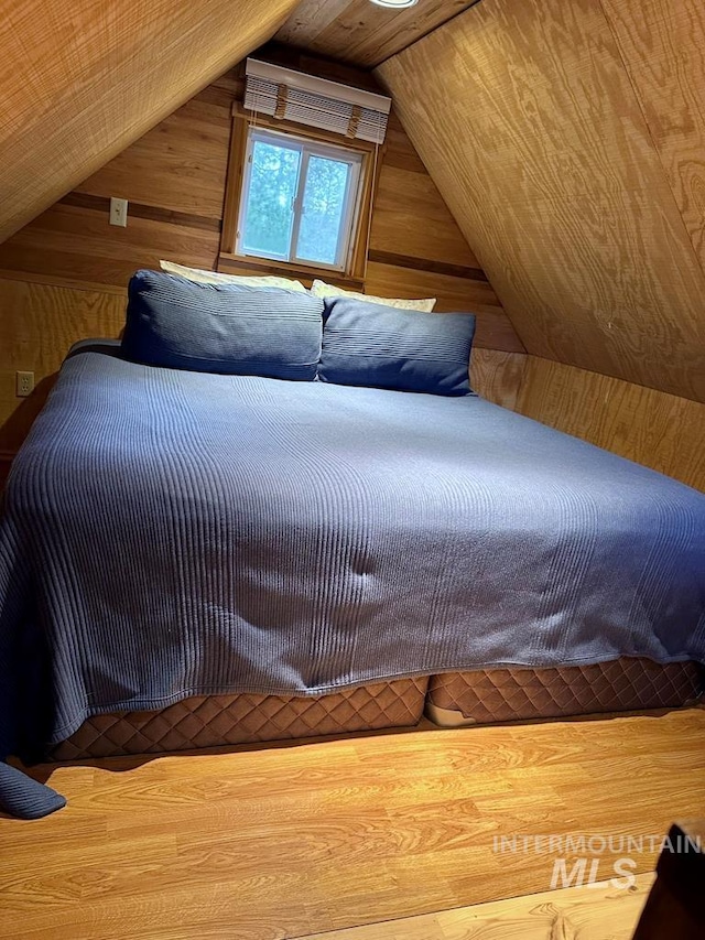 bedroom featuring vaulted ceiling and wooden walls